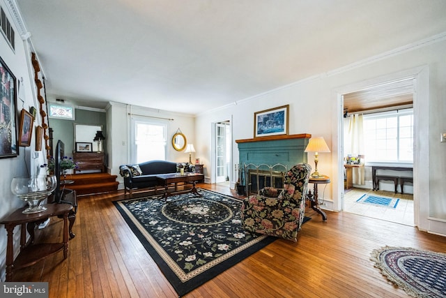 living area with visible vents, a brick fireplace, hardwood / wood-style flooring, and crown molding