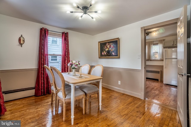 dining area featuring radiator heating unit, baseboard heating, plenty of natural light, and hardwood / wood-style floors