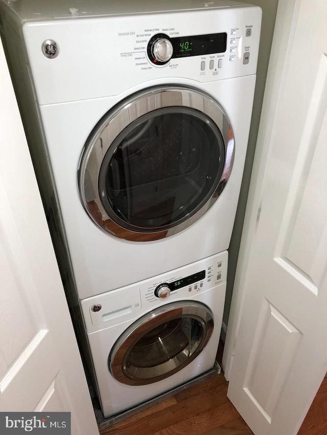 clothes washing area featuring dark hardwood / wood-style floors and stacked washer / drying machine