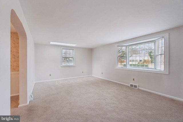 spare room featuring light colored carpet, visible vents, arched walkways, and baseboards