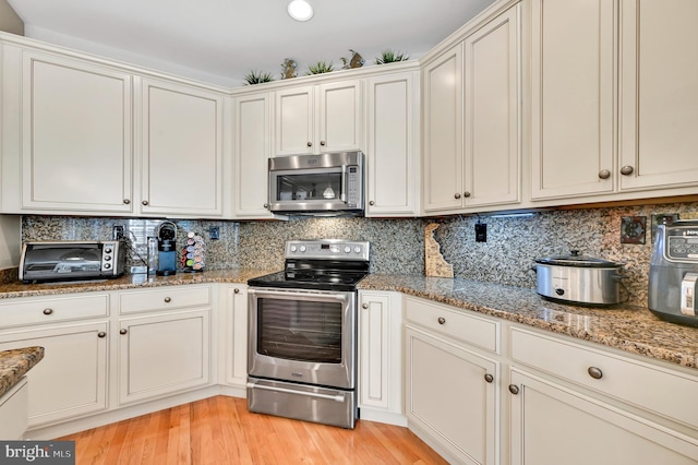 kitchen with light wood-type flooring, tasteful backsplash, stone counters, appliances with stainless steel finishes, and white cabinets