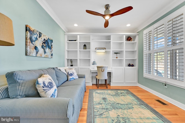 living room featuring ceiling fan, light wood-type flooring, crown molding, and built in desk