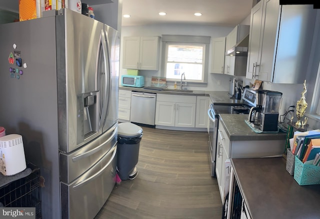 kitchen with dark wood-type flooring, stainless steel appliances, wall chimney range hood, white cabinetry, and a sink