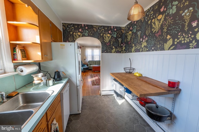 kitchen with a sink, light countertops, hanging light fixtures, wainscoting, and wallpapered walls