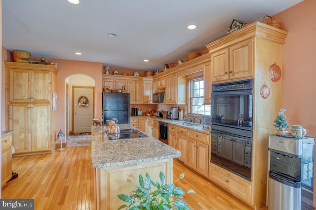 kitchen featuring light stone counters, black appliances, light brown cabinets, a kitchen island, and sink