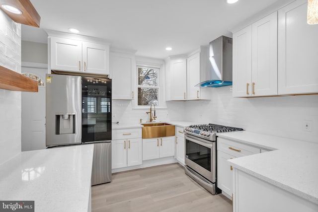 kitchen featuring appliances with stainless steel finishes, white cabinetry, a sink, and wall chimney exhaust hood