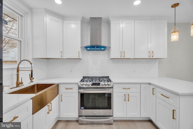 kitchen featuring a sink, white cabinetry, stainless steel gas stove, wall chimney exhaust hood, and decorative light fixtures