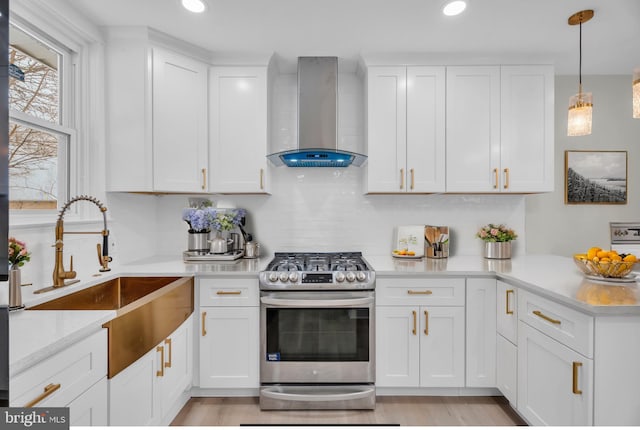 kitchen featuring pendant lighting, white cabinets, a sink, gas range, and wall chimney exhaust hood