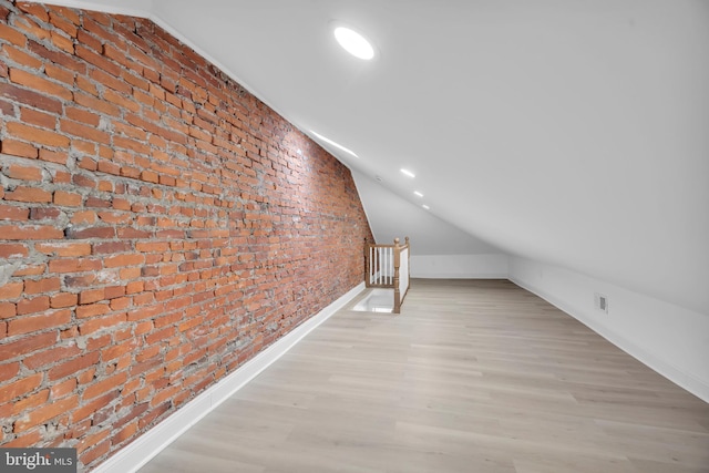 bonus room featuring light wood-type flooring, lofted ceiling, brick wall, and recessed lighting