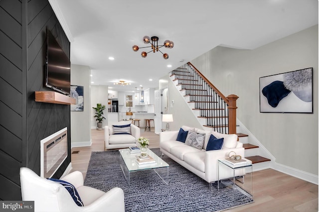 living room with recessed lighting, a fireplace, stairs, light wood finished floors, and an inviting chandelier