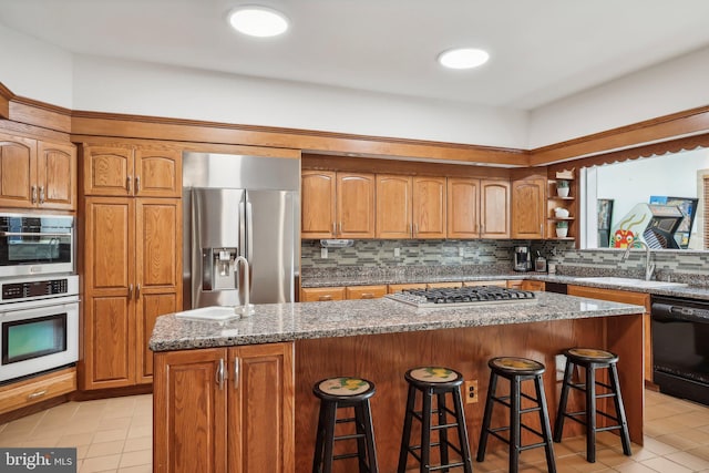 kitchen with appliances with stainless steel finishes, sink, a kitchen bar, and a center island