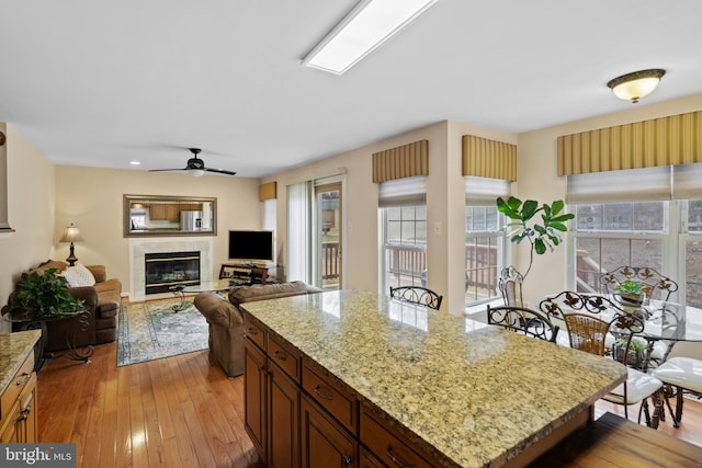 kitchen with light wood-style floors, a glass covered fireplace, a ceiling fan, and light stone countertops