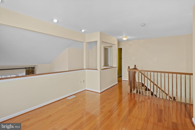 spare room featuring lofted ceiling, baseboards, visible vents, and hardwood / wood-style floors