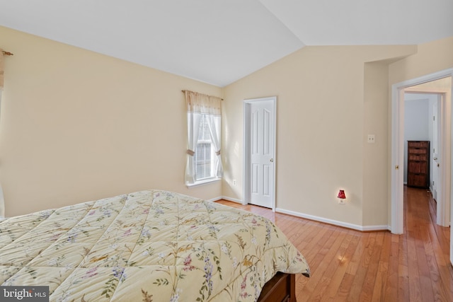 bedroom with light wood-type flooring, lofted ceiling, a closet, and baseboards