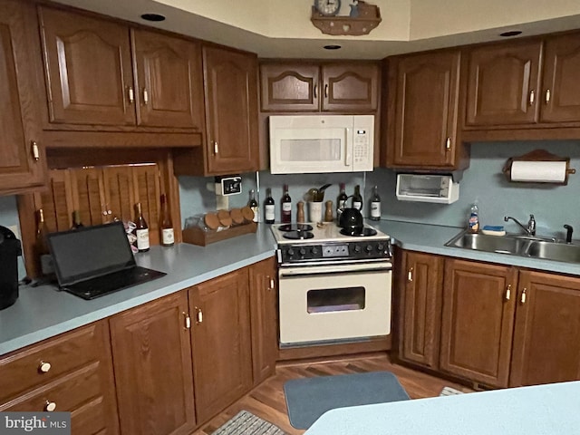 kitchen with light countertops, white appliances, a sink, and brown cabinets