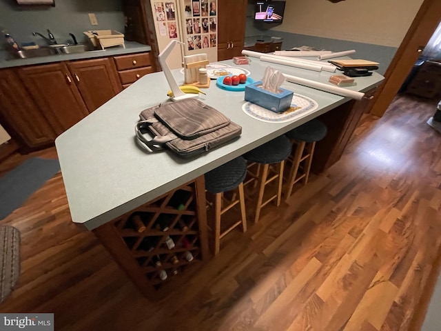 kitchen featuring wood finished floors, a kitchen bar, a sink, and brown cabinets