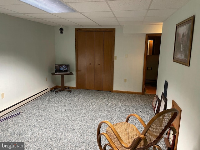 interior space with carpet floors, a baseboard heating unit, a drop ceiling, and baseboards