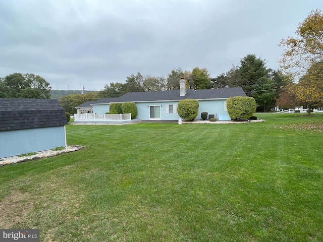 back of house featuring a yard, an outdoor structure, a chimney, and a storage shed