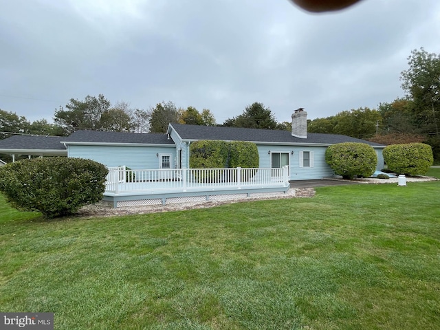 rear view of property with a lawn, a chimney, and a wooden deck