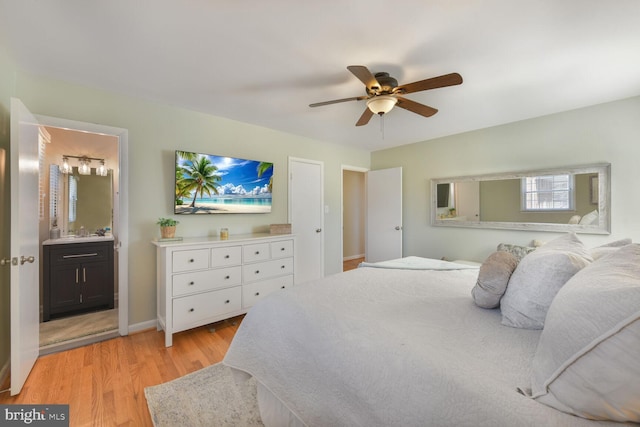 bedroom featuring ceiling fan, a sink, baseboards, light wood-type flooring, and ensuite bath