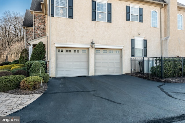 exterior space with aphalt driveway, an attached garage, fence, stone siding, and stucco siding