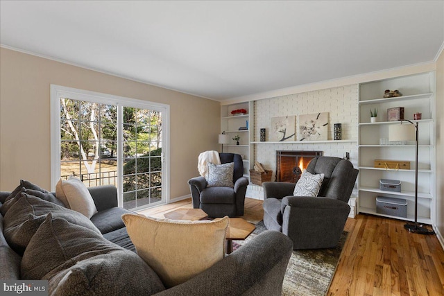 living area with built in shelves, a fireplace, wood finished floors, and crown molding