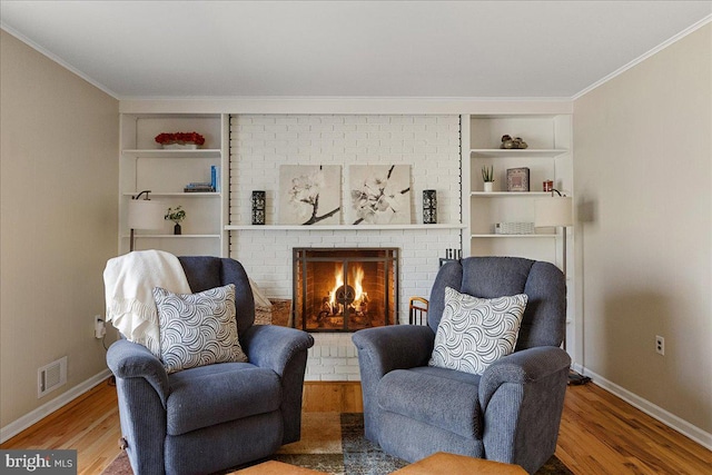 living area featuring built in shelves, ornamental molding, a fireplace, and wood finished floors