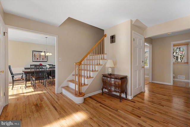 stairway with visible vents, baseboards, a chandelier, and wood finished floors