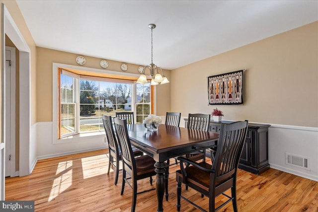 dining area featuring light wood finished floors, baseboards, visible vents, and an inviting chandelier