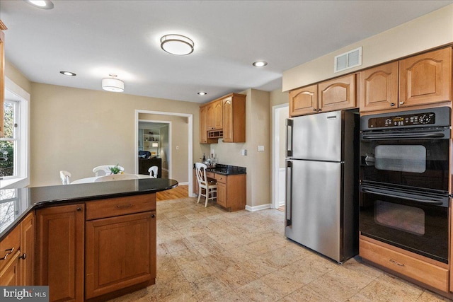 kitchen with dark countertops, dobule oven black, visible vents, brown cabinetry, and freestanding refrigerator