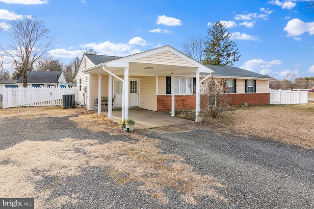 view of front of property featuring an attached carport, fence, central AC unit, and brick siding