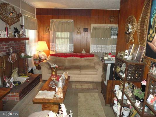 living room featuring a brick fireplace and wooden walls