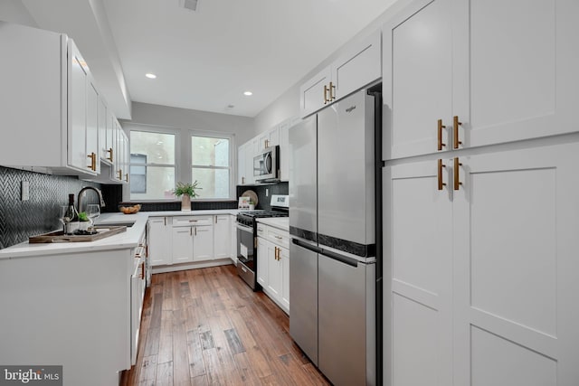 kitchen with a sink, white cabinetry, light countertops, appliances with stainless steel finishes, and backsplash