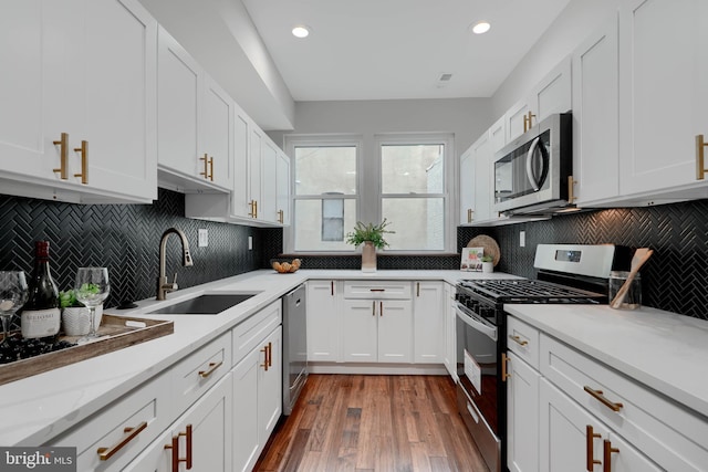 kitchen with wood finished floors, a sink, white cabinets, appliances with stainless steel finishes, and light stone countertops