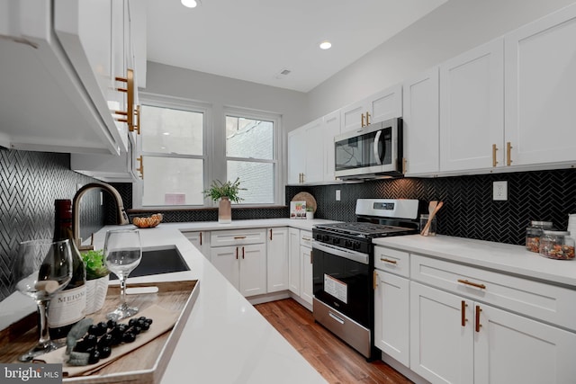 kitchen featuring stainless steel appliances, a sink, white cabinets, light countertops, and decorative backsplash