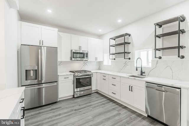 kitchen with white cabinets, appliances with stainless steel finishes, sink, and light stone countertops