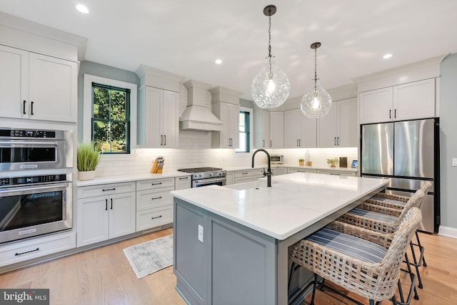 kitchen with a kitchen island with sink, stainless steel appliances, sink, custom exhaust hood, and a breakfast bar area