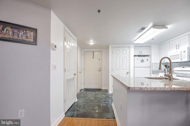 kitchen featuring white appliances, visible vents, white cabinets, light stone countertops, and a sink