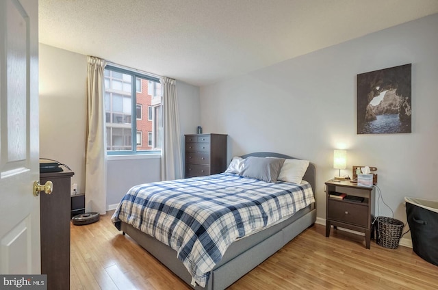 bedroom featuring a textured ceiling, light wood-type flooring, and baseboards