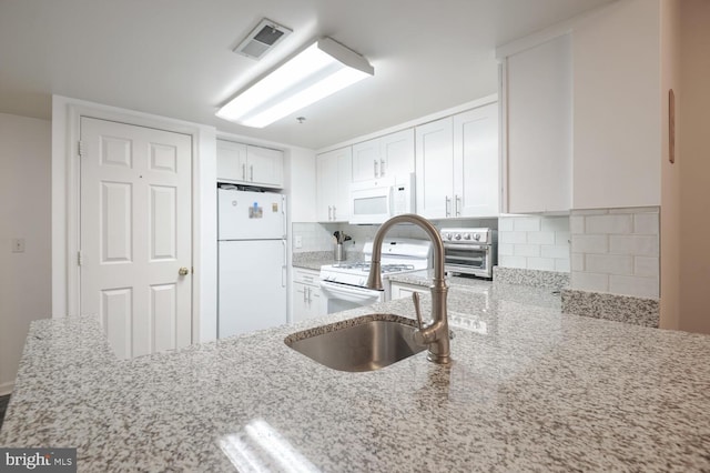 kitchen featuring light stone counters, white appliances, visible vents, white cabinetry, and backsplash