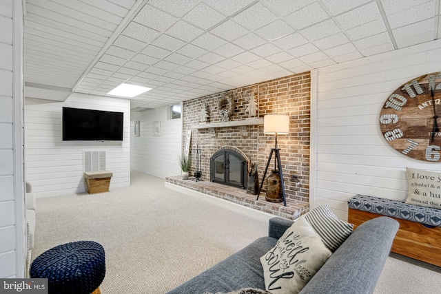 carpeted living area featuring a drop ceiling, a fireplace, and wooden walls