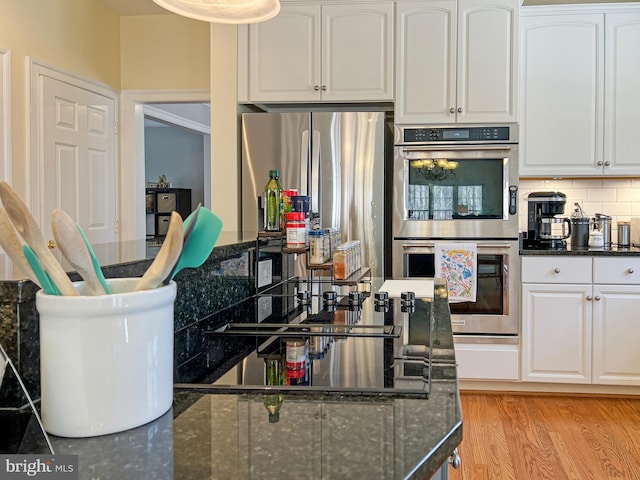 kitchen with tasteful backsplash, white cabinets, dark stone countertops, stainless steel appliances, and light wood-type flooring