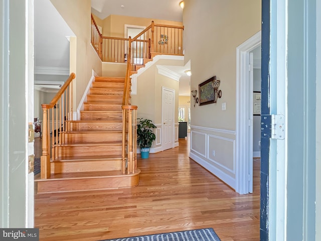 entryway with a decorative wall, a wainscoted wall, a high ceiling, wood finished floors, and stairs