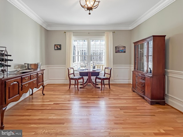 dining room with light wood-type flooring, a wainscoted wall, a decorative wall, and crown molding