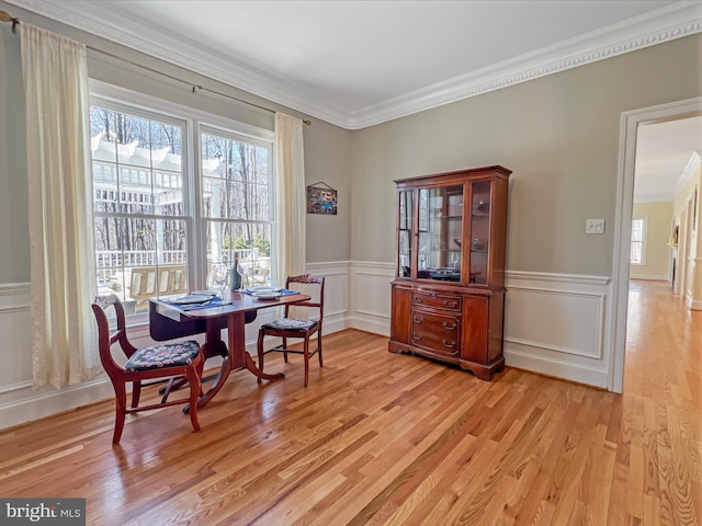 dining room with wainscoting, crown molding, light wood-style flooring, and a decorative wall