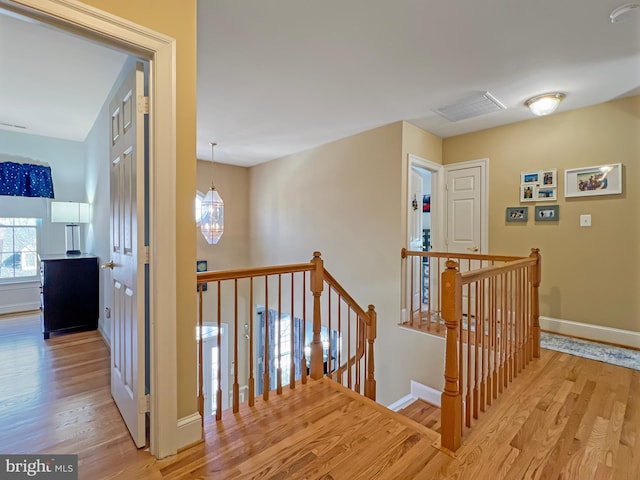 corridor with an inviting chandelier, light wood-type flooring, an upstairs landing, and baseboards