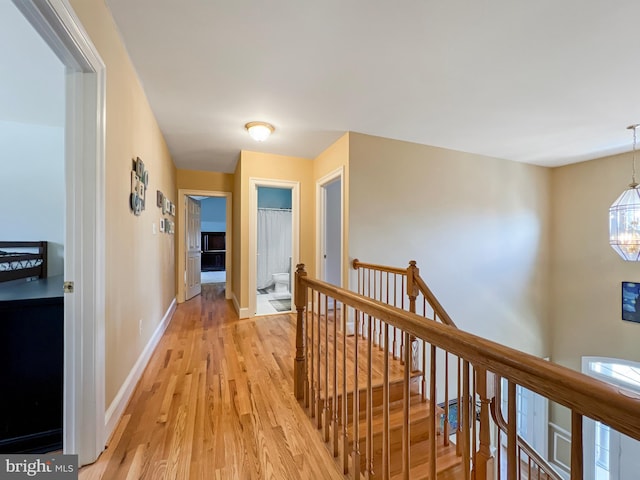 hallway featuring light wood-style floors, baseboards, a notable chandelier, and an upstairs landing