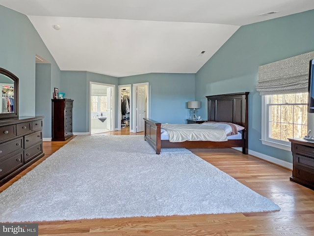 bedroom featuring lofted ceiling, multiple windows, light wood-style flooring, and baseboards