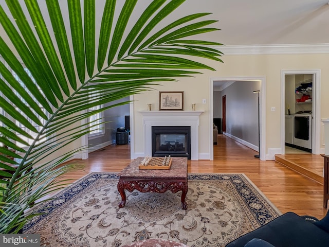 living room featuring light wood-style flooring, baseboards, ornamental molding, a glass covered fireplace, and washer / dryer