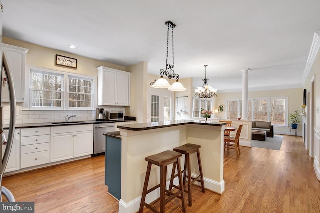 kitchen featuring a breakfast bar, white cabinets, appliances with stainless steel finishes, dark countertops, and pendant lighting